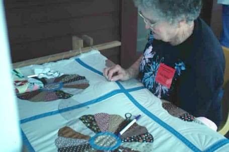Nova Mercer of Jonesboro uses a frame supported by wooden saw horses to quilt the three layers of quilt together.
